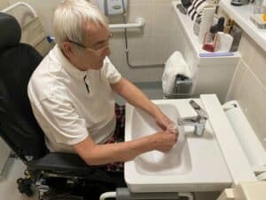 Man in powerchair washes hands at Ropox QuickWash basin.